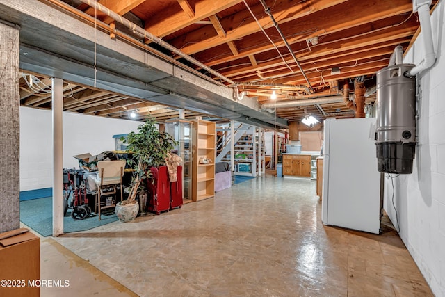 unfinished basement with freestanding refrigerator and stairs
