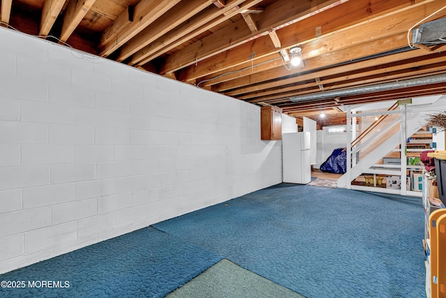 unfinished below grade area featuring freestanding refrigerator and stairs