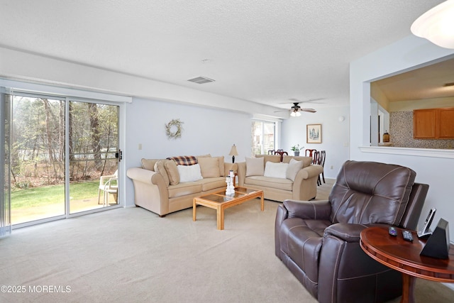 living area with visible vents, light carpet, a textured ceiling, and ceiling fan