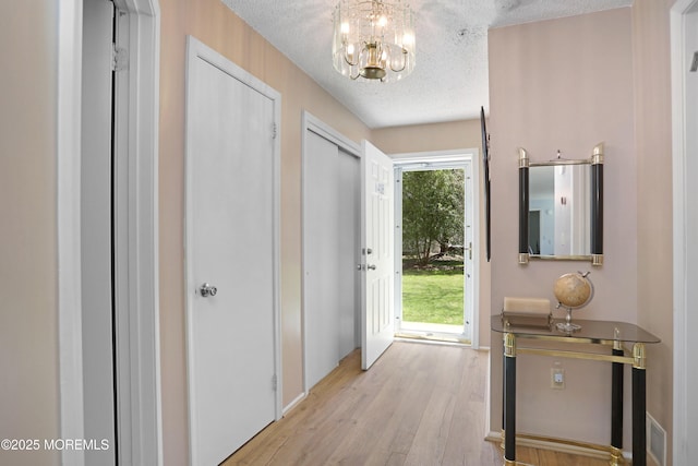 doorway to outside featuring an inviting chandelier, a textured ceiling, and light wood-style flooring