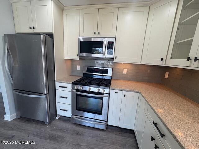 kitchen featuring tasteful backsplash, glass insert cabinets, appliances with stainless steel finishes, white cabinets, and dark wood-style flooring
