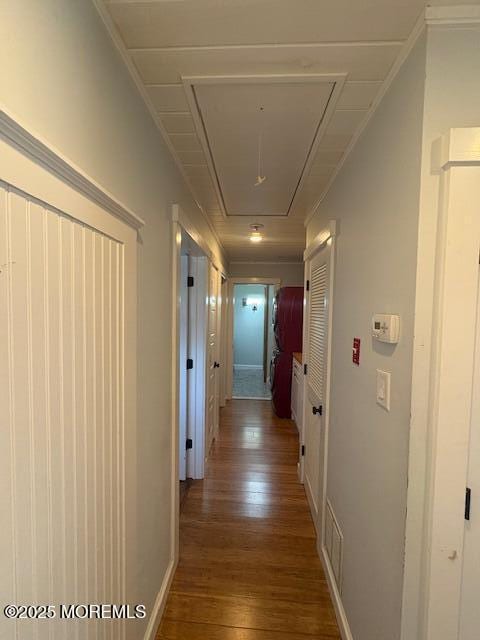 hall featuring baseboards, visible vents, attic access, and wood finished floors