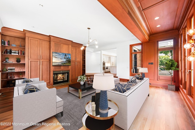 living area with crown molding, an inviting chandelier, light wood-style flooring, and a warm lit fireplace