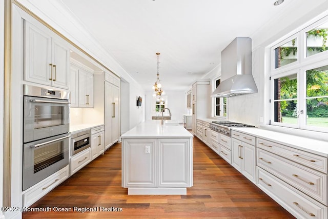 kitchen featuring stainless steel appliances, dark wood-type flooring, white cabinetry, wall chimney range hood, and light countertops
