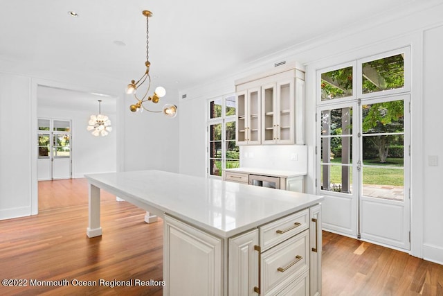 kitchen with an inviting chandelier, light wood-style floors, glass insert cabinets, a center island, and light countertops
