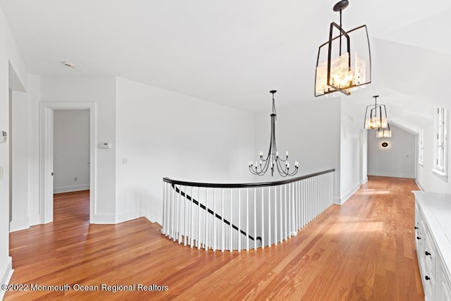 corridor featuring a chandelier, baseboards, an upstairs landing, and light wood finished floors