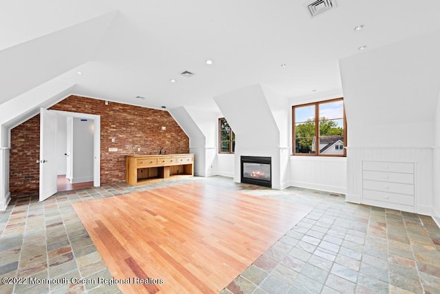 unfurnished living room with lofted ceiling, stone tile floors, visible vents, and brick wall