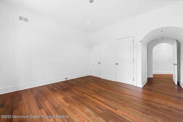 spare room with arched walkways, wood finished floors, baseboards, visible vents, and crown molding