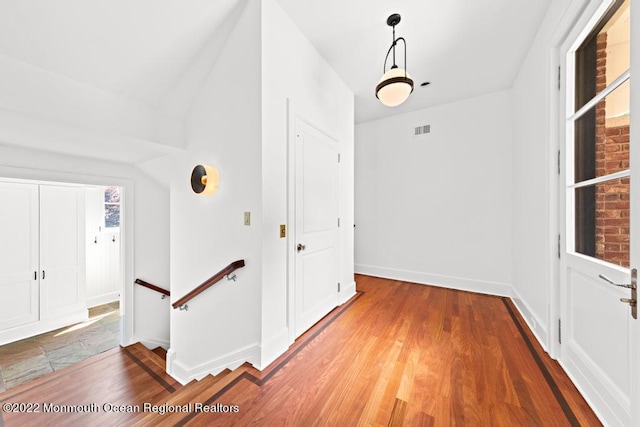 hall with an upstairs landing, wood finished floors, visible vents, and baseboards