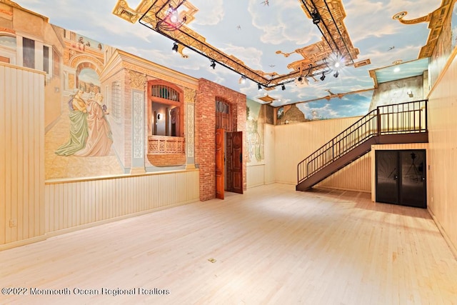 unfurnished living room featuring wallpapered walls, wood finished floors, a wainscoted wall, and stairs