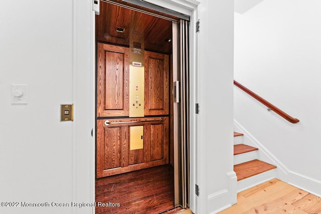 stairway featuring baseboards, wood finished floors, and elevator