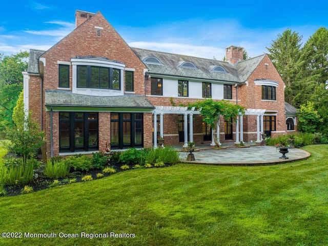 rear view of property featuring a chimney, a patio area, a pergola, a lawn, and brick siding
