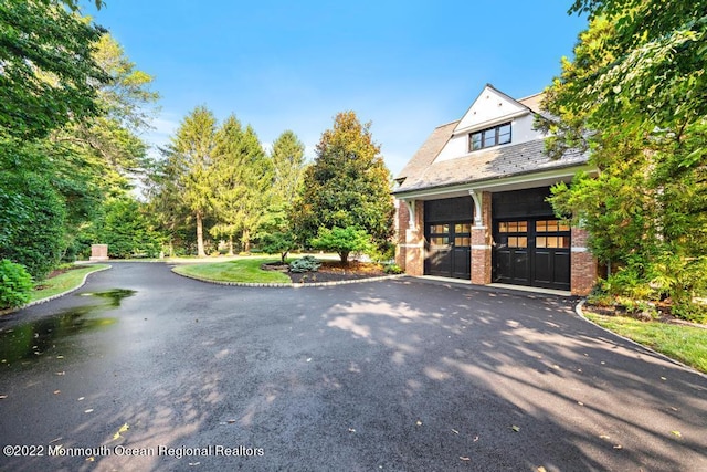 view of side of home featuring brick siding, aphalt driveway, a high end roof, and an attached garage