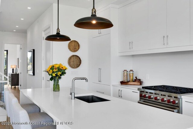 kitchen featuring light countertops, white cabinets, high end stove, and a sink