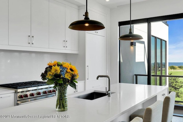 kitchen featuring hanging light fixtures, stainless steel range, a kitchen bar, a sink, and white cabinetry