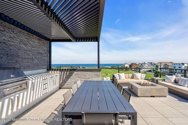 view of patio with an outdoor kitchen, an outdoor living space with a fire pit, a water view, and a grill