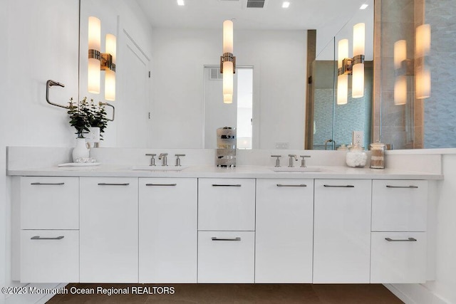 bathroom with visible vents, a shower with shower door, double vanity, and a sink