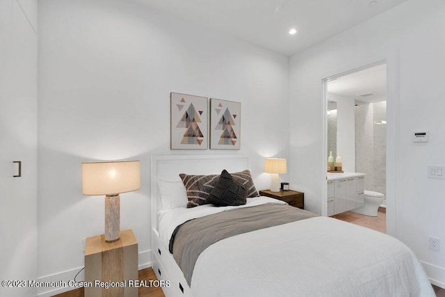 bedroom featuring wood finished floors, ensuite bath, and baseboards