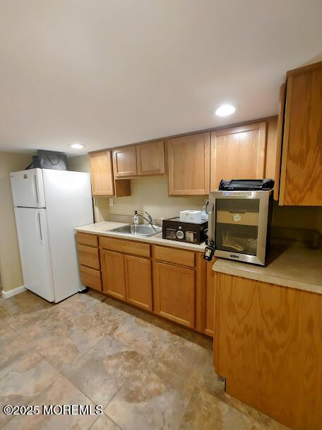 kitchen with a sink, light countertops, freestanding refrigerator, and recessed lighting