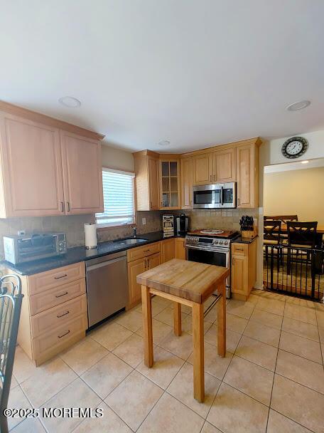 kitchen with a sink, decorative backsplash, light tile patterned floors, and stainless steel appliances