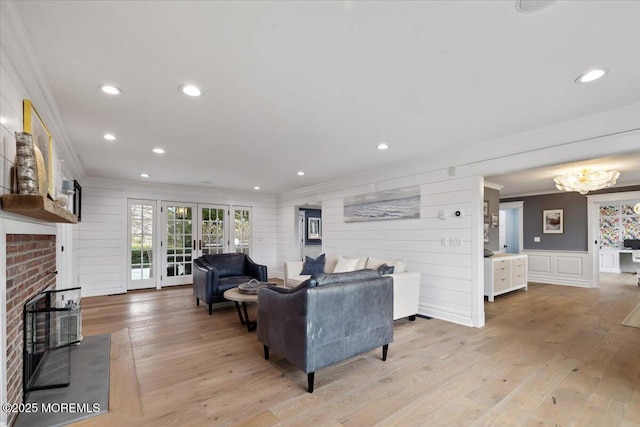 living area featuring light wood-type flooring, ornamental molding, french doors, and a fireplace
