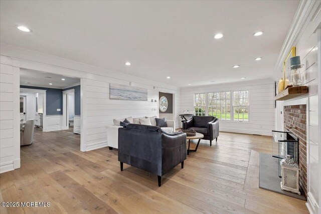 living area featuring a fireplace, light wood-style floors, crown molding, and recessed lighting