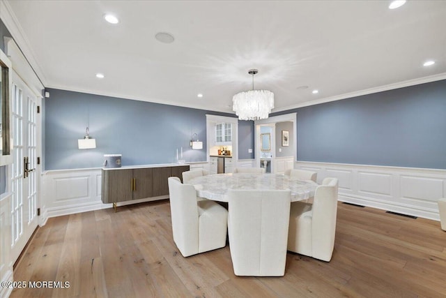 dining area with crown molding, visible vents, a wainscoted wall, an inviting chandelier, and a decorative wall