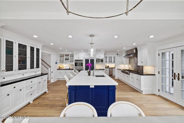 kitchen featuring stainless steel appliances, a sink, white cabinetry, wall chimney exhaust hood, and french doors