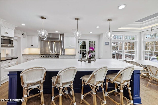 kitchen with stainless steel microwave, tasteful backsplash, wall chimney exhaust hood, white cabinetry, and blue cabinets
