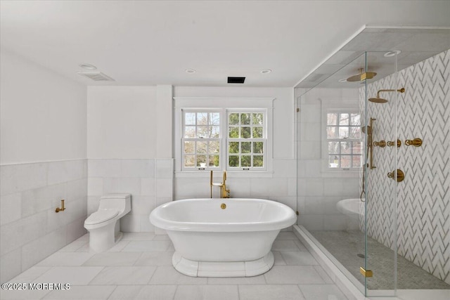 bathroom featuring tile walls, a freestanding tub, tile patterned floors, toilet, and a stall shower