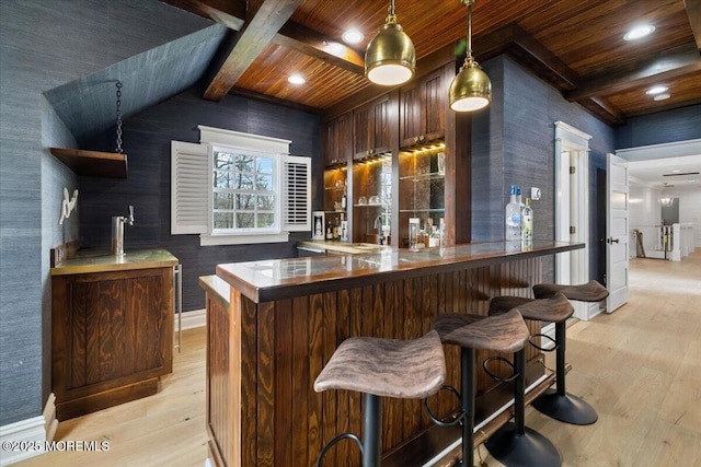 bar featuring indoor wet bar, baseboards, light wood finished floors, and wooden ceiling