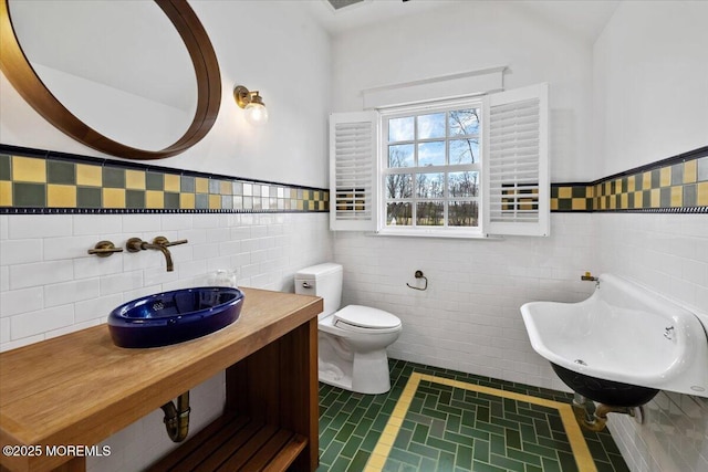 half bathroom featuring tile walls, a wainscoted wall, toilet, and a sink