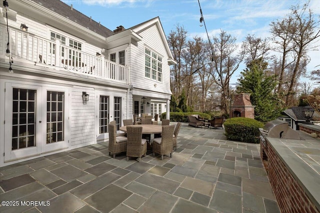 view of patio with a fireplace, a balcony, outdoor dining space, an outdoor kitchen, and french doors