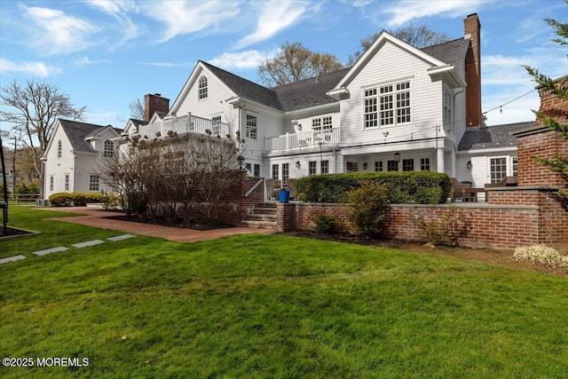 back of property with a chimney, a balcony, and a lawn