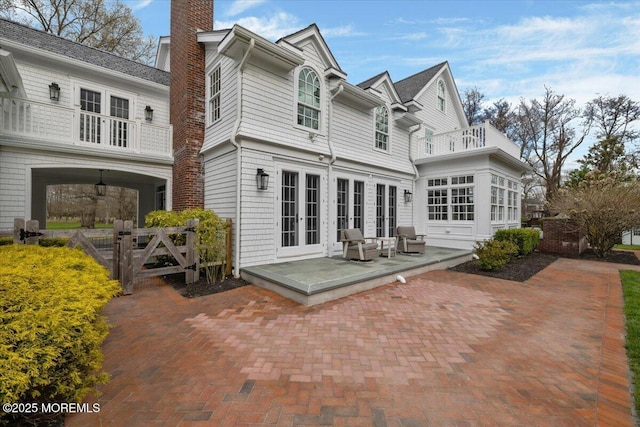 back of property featuring a chimney, french doors, a balcony, and a patio