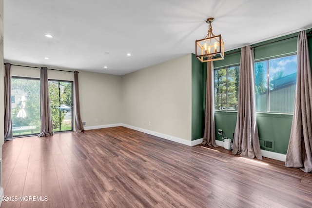 unfurnished room with an inviting chandelier, baseboards, wood finished floors, and visible vents