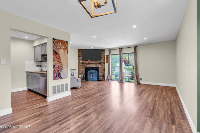 unfurnished living room with visible vents, a large fireplace, wood finished floors, a sink, and an inviting chandelier