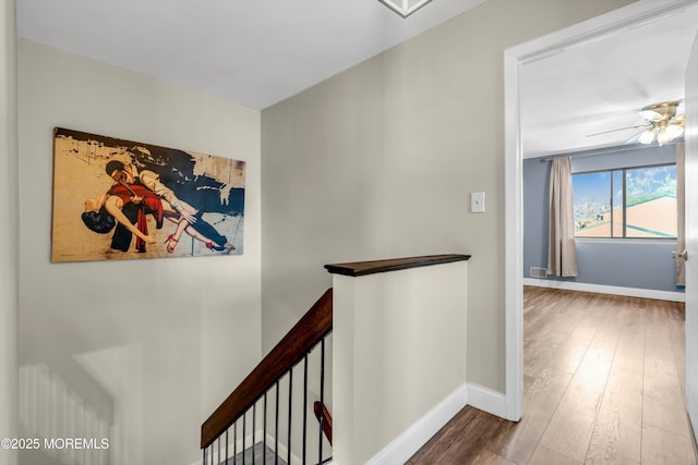 corridor featuring baseboards, an upstairs landing, and wood finished floors