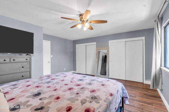 bedroom with wood finished floors, a ceiling fan, baseboards, and two closets