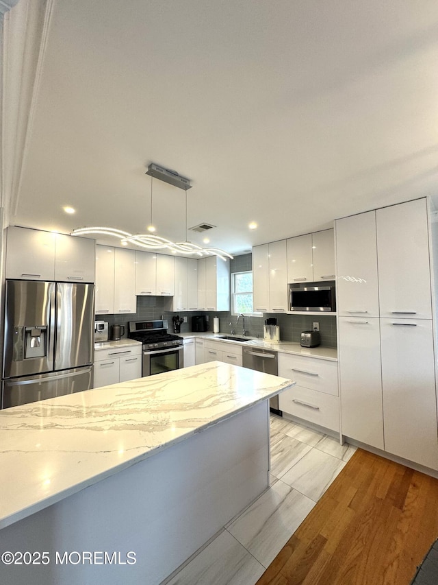 12 Yates Ave, South River, NJ 08882 - kitchen with stainless steel appliances, modern cabinets, white cabinets, light stone counters, and hanging light fixtures