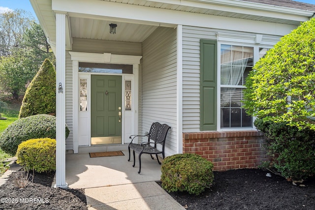 doorway to property with covered porch and brick siding