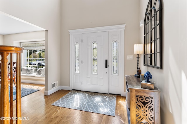 entryway with baseboards, a high ceiling, wood finished floors, and visible vents