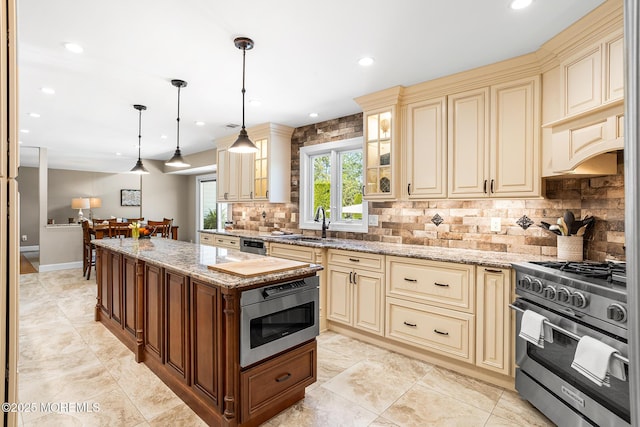 kitchen featuring decorative backsplash, cream cabinetry, light stone counters, a sink, and high end stainless steel range oven