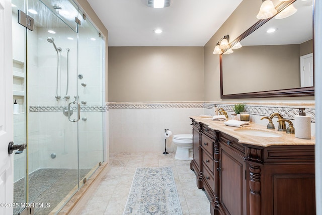 bathroom featuring vanity, wainscoting, toilet, tile walls, and a shower stall