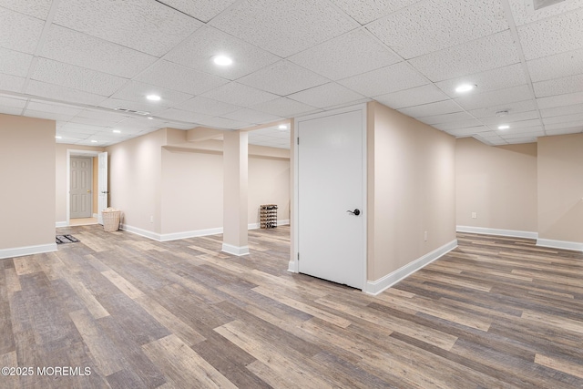 finished below grade area featuring baseboards, recessed lighting, a drop ceiling, and wood finished floors