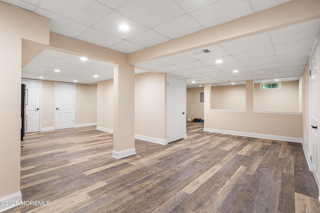 finished basement with visible vents, baseboards, a paneled ceiling, and wood finished floors
