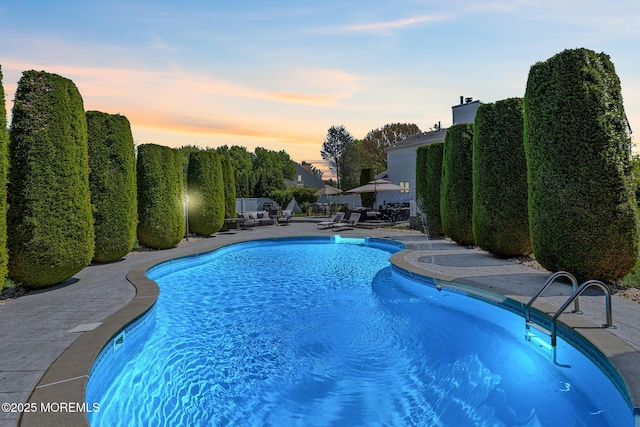 pool at dusk featuring a patio area and an outdoor pool