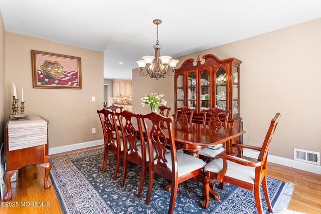 dining area with an inviting chandelier, baseboards, wood finished floors, and visible vents