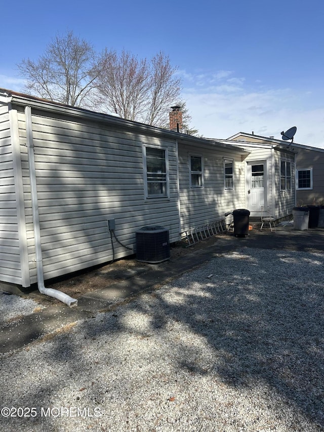 back of house featuring central AC and a chimney