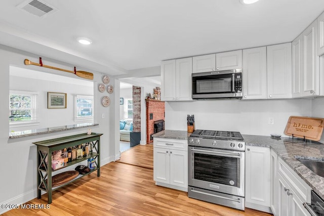 4 W Lake Rd, Red Bank, NJ 07701 - kitchen with stainless steel appliances, white cabinets, light wood finished floors, light stone counters, and baseboards